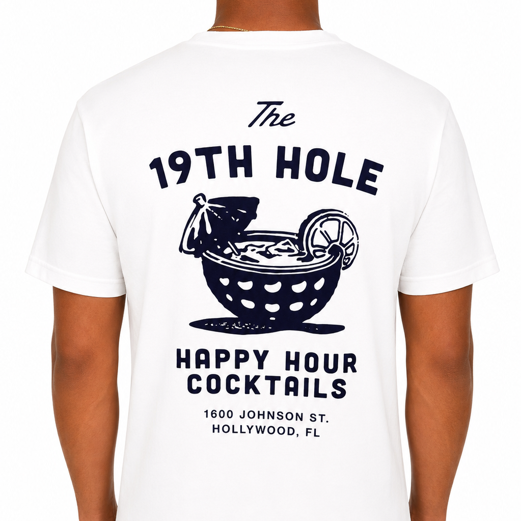 Male model shown from the back wearing a white Sandtrap t-shirt featuring a large black graphic that reads “The 19th Hole Happy Hour Cocktails” with a golf ball-style cocktail bowl illustration and location text beneath. Studio product image on a clean white background.