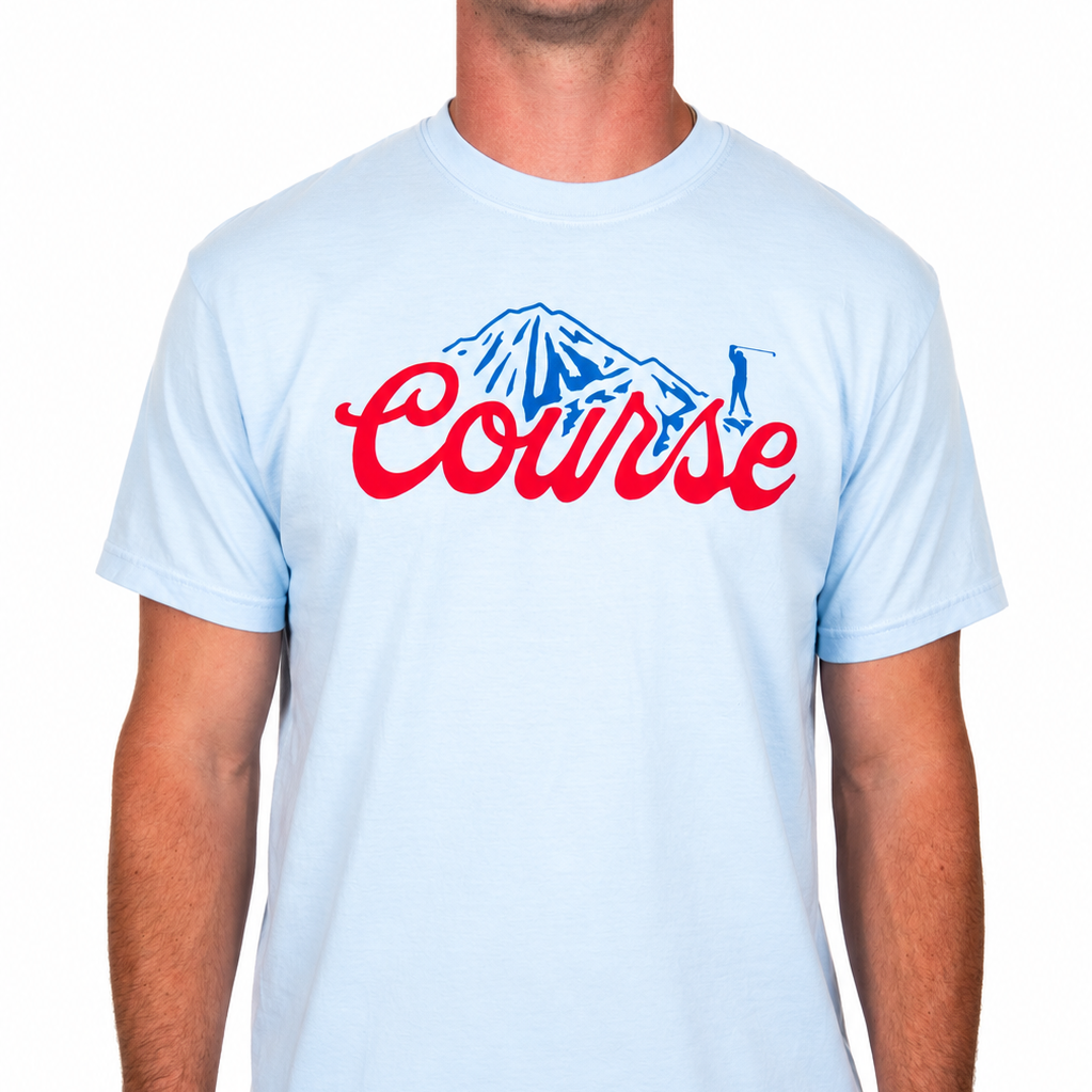 Male model wearing a light blue Sandtrap T-shirt featuring a bold red "Course" script graphic with a blue mountain and golfer illustration across the chest. Shown from the front against a clean white studio background.
