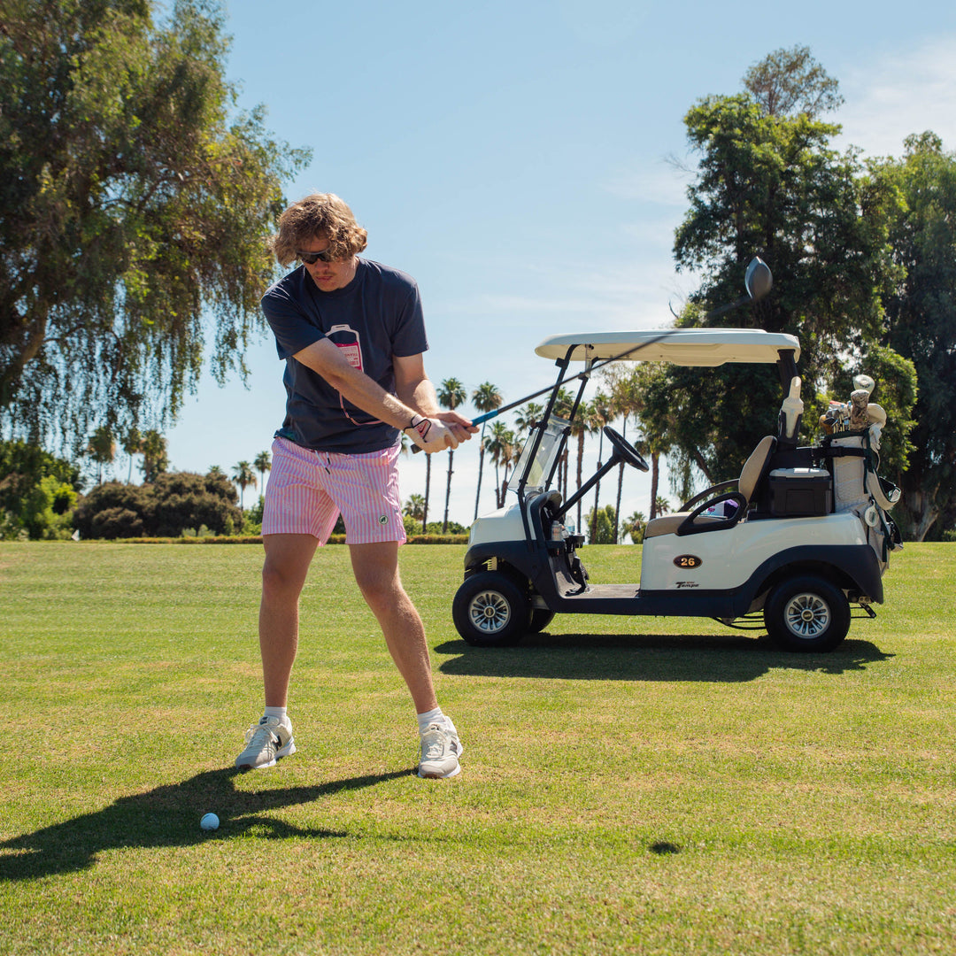 Male model playing golf on a sunny day with a golf cart in the background wearing transfusion IV bag graphic centered on the chest with tubing extending across the lower front.