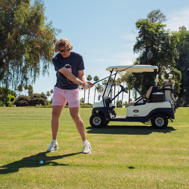 Male model playing golf on a sunny day with a golf cart in the background wearing transfusion IV bag graphic centered on the chest with tubing extending across the lower front.