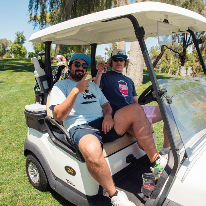 Two people in a golf cart on a golf course with palm trees in the background.