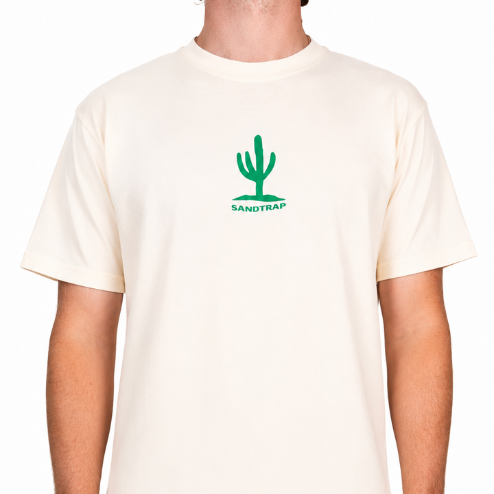 Male model wearing a cream Sandtrap T-shirt featuring a small front chest cactus graphic. The relaxed-fit tee is shown against a clean studio background.