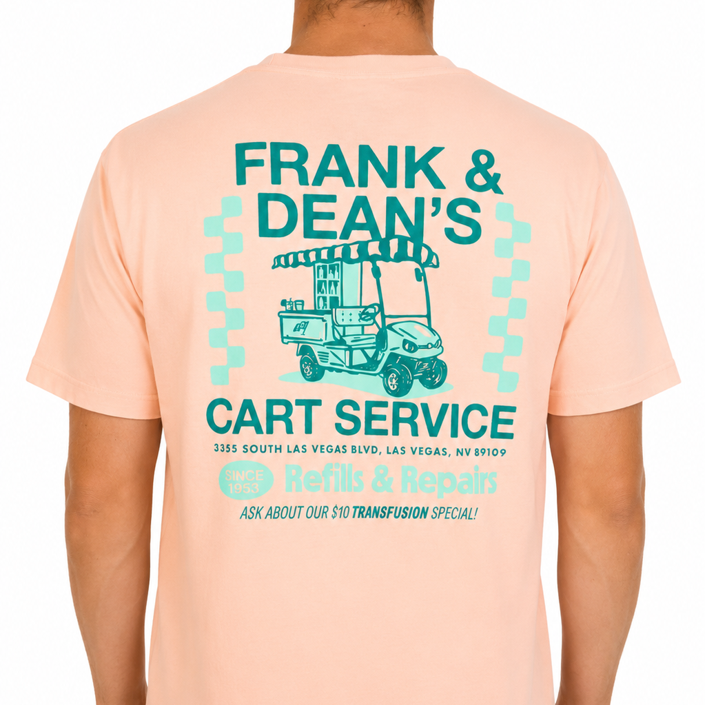 Male model wearing a peach Sandtrap T-shirt featuring a large “Frank &amp; Dean’s Cart Service” graphic across the back. The retro-inspired artwork includes a vintage golf cart illustration, teal and mint green lettering, and repair shop-style details, showcased against a clean studio background to highlight the fit and back graphic.