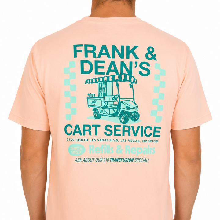 Male model wearing a peach Sandtrap T-shirt featuring a large “Frank &amp; Dean’s Cart Service” graphic across the back. The retro-inspired artwork includes a vintage golf cart illustration, teal and mint green lettering, and repair shop-style details, showcased against a clean studio background to highlight the fit and back graphic.