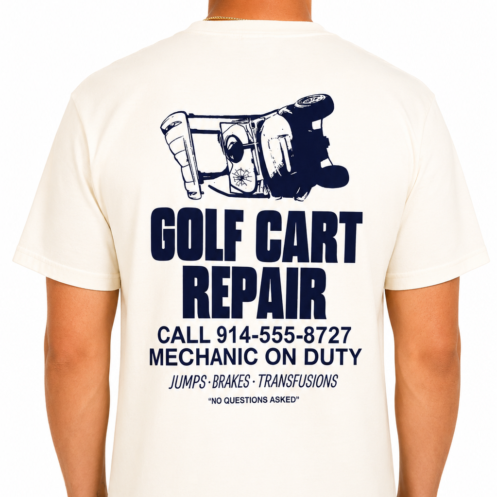 Male model wearing a cream Sandtrap Golf short-sleeve t-shirt featuring a large navy "Golf Cart Repair" graphic on the back with an overturned golf cart illustration and vintage repair shop-inspired text. Relaxed fit shown against a clean white studio background.