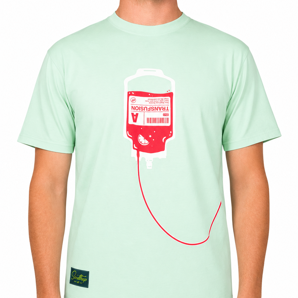 Front view of a male model wearing a mint green graphic t-shirt against a clean white studio background. The t-shirt features a large transfusion IV bag graphic in pink and white centered on the chest, with tubing extending across the lower front of the shirt.